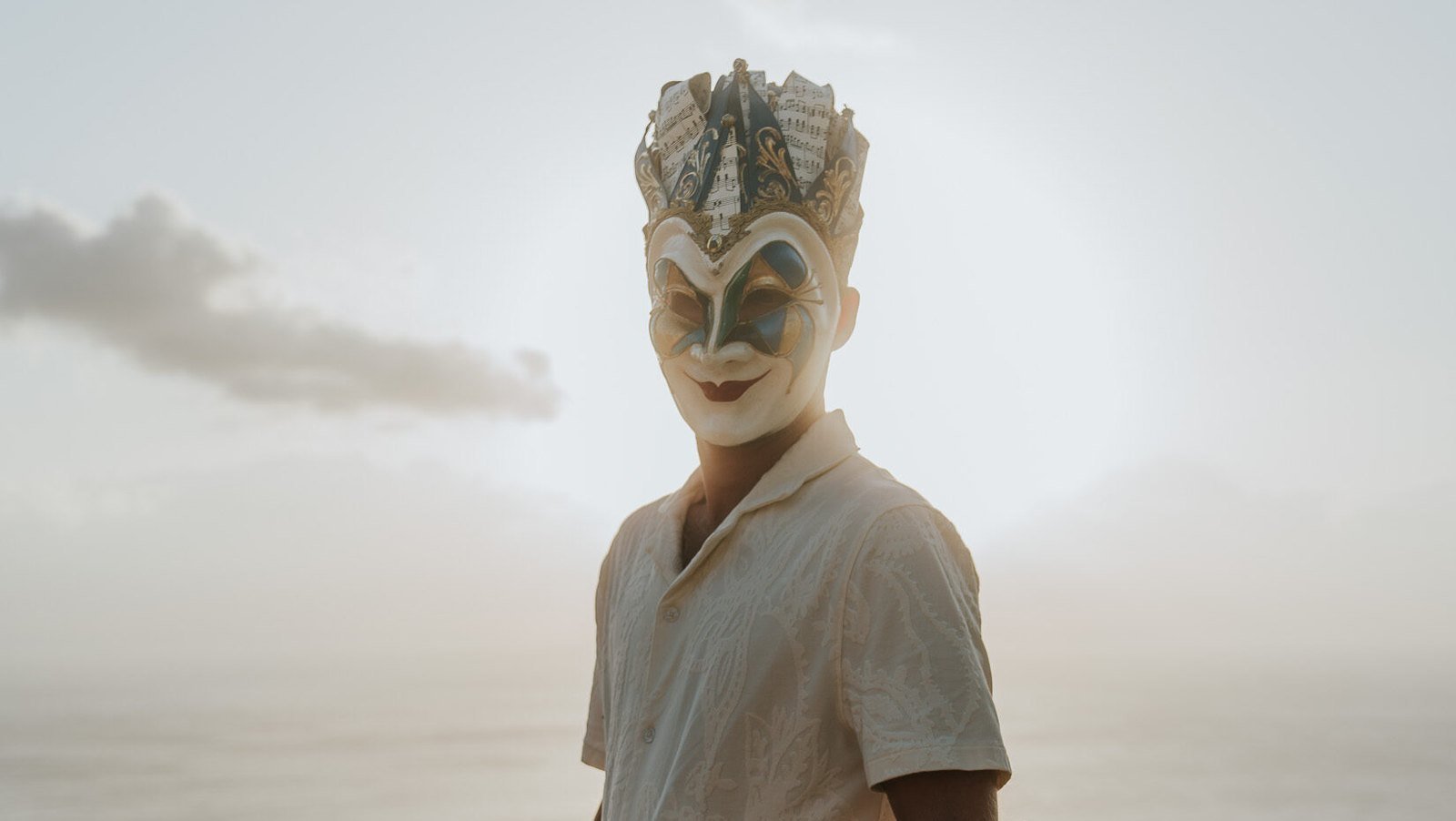 Boris Brejcha in his Joker mask with a sheet-music crown and a cream patterned shirt, against a hazy sky; his farewell tour follows in 2028.