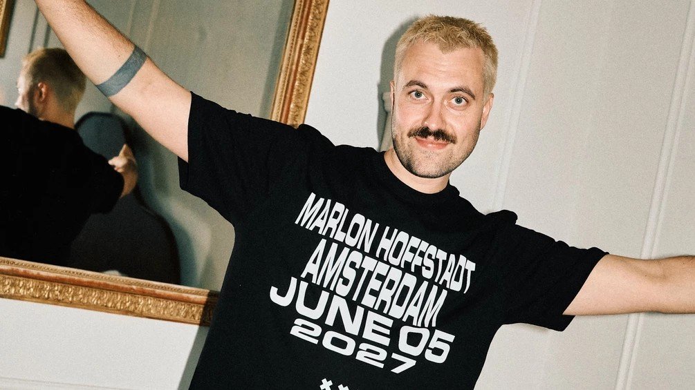 Marlon Hoffstadt with his arms spread, wearing a T-shirt for his Amsterdam open air that reads Marlon Hoffstadt Amsterdam June 05 2027.